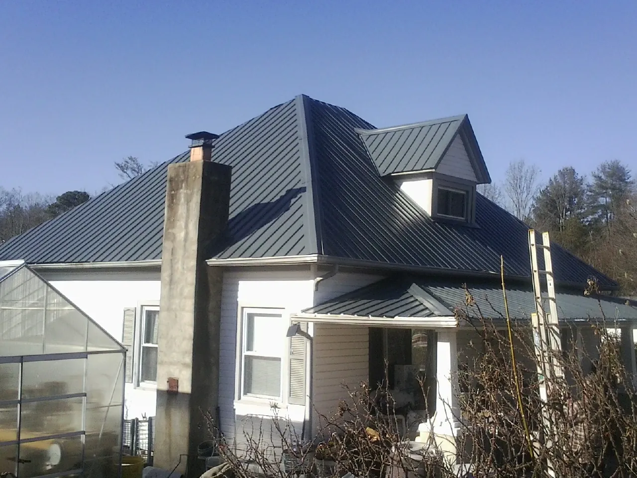 Dark blue standing seam metal roof on a white farmhouse with dormer — Slate & Tile Roof Repair by Roofing Brothers in Bennett
