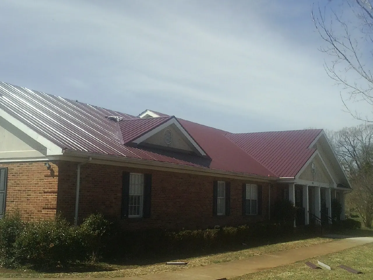 Red metal roof with gabled entries on a long brick building, from a Hail Damage Roof Repair job in Bennett