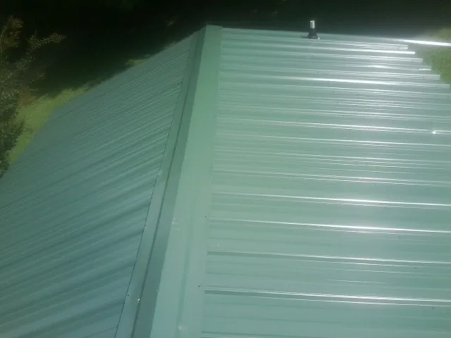 New green metal panels meeting at the ridge of a roof — Flat Roof Repair work by our crew in Bennett